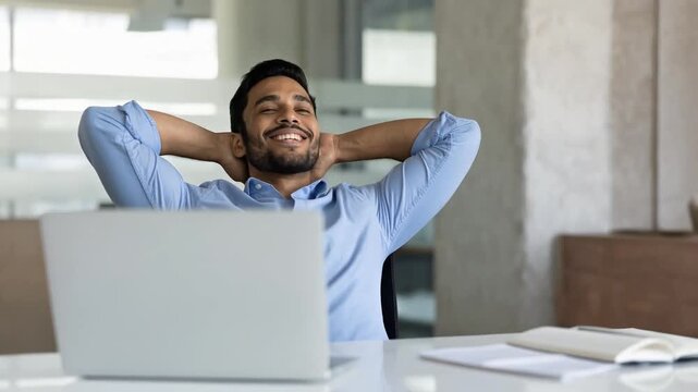 Smiling professional man relaxing at office desk showing satisfaction after completing work