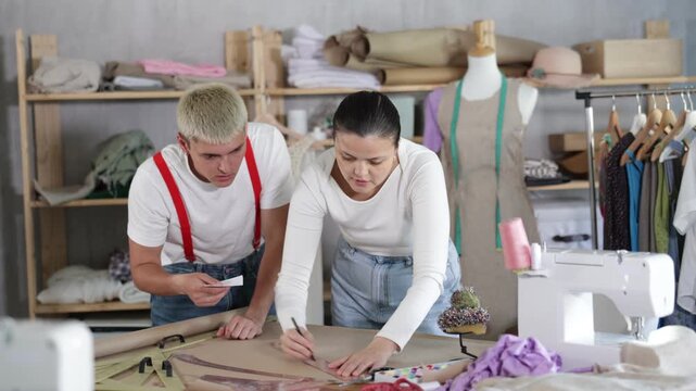 Team of tailors work together in the workshop, they draw a layout on paper, discuss edits and the concept of the clothing collection. Process of working on a sample of clothes for a client. High