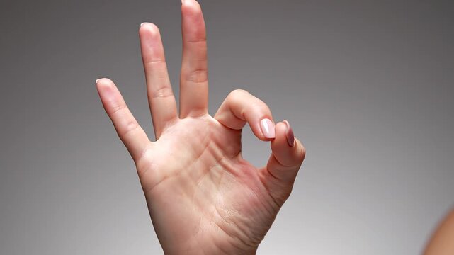 Female hand forming okay sign with fingers isolated on neutral background in studio light