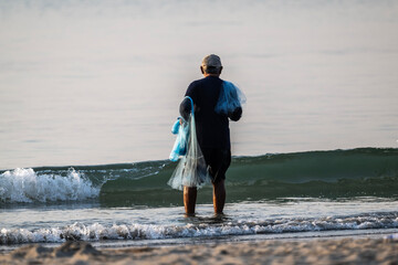 A Thai fisherman with a net catches fish in the coastal area on a sunny morning © константин константи