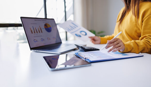 Cusiness woman thinking, calculating, looking at financial statements and planning marketing, reviewing documents, calculating numbers, recording data on laptop online in office.
