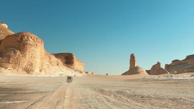 Distant view off road vehicle driving on sand in Sahara desert with high limestone rock formations in the horizon