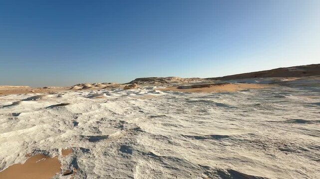 Low angle motion along textured white stone ground with sand channels in the desert