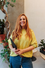 Confident businesswoman in a yellow sweater at a Madrid coworking space, smiling with folder