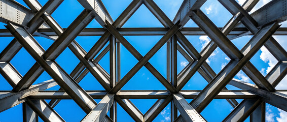 Fototapeta premium Industrial skeletal structure and steel construction framework at twilight with prominent architectural metal beams viewed from below against a blue sky