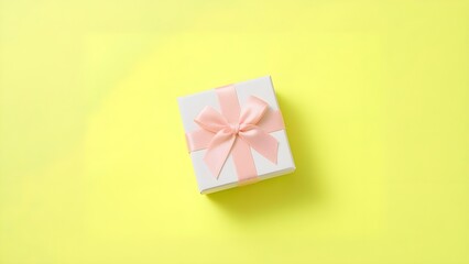 Beautifully wrapped white gift box with elegant pink ribbon on bright yellow background
