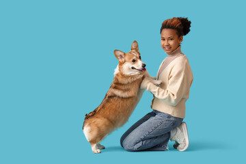 Obraz premium Teenage African-American girl hugging Corgi dog on blue background