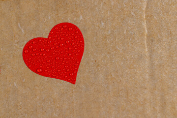 Fototapeta premium wet hard yellow cardboard for packaging goods and products with red plastic hearts glued on , a piece of corrugated cardboard with one red heart covered with water droplets