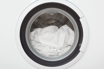White bed sheet in closed washing machine. Clothes care. Closeup. Front view.