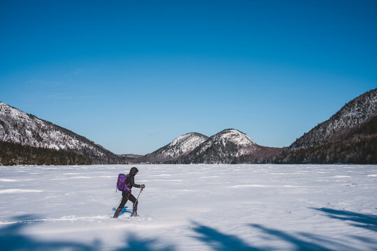 Female hikes across frozen Jordan Pond in Acadia on frigid winter day.