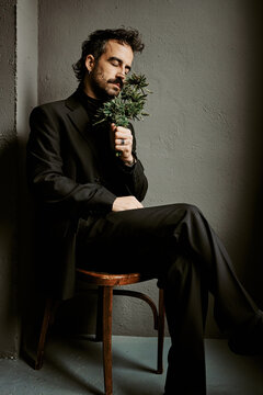 Elegant man in suit smelling fresh cannabis plant in dark studio