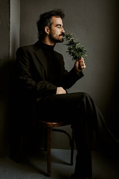 Elegant man in suit smelling fresh cannabis plant in dark studio