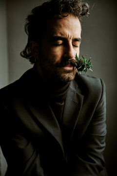 Elegant man in suit smelling fresh cannabis plant in dark studio