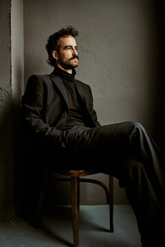 Pensive man in black suit sitting alone in dramatic shadows