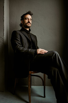 Pensive man in black suit sitting alone in dramatic shadows
