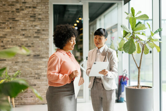 Businesswomen discussing work with tablet and documents in modern office