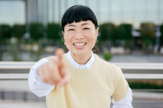 Smiling woman pointing at camera outdoors in urban lifestyle setting