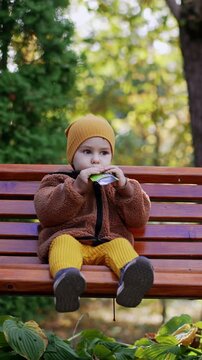 Beautiful Caucasian kid eating fruit puree from doypack. Healthy snack during walk in the park. Vertical video