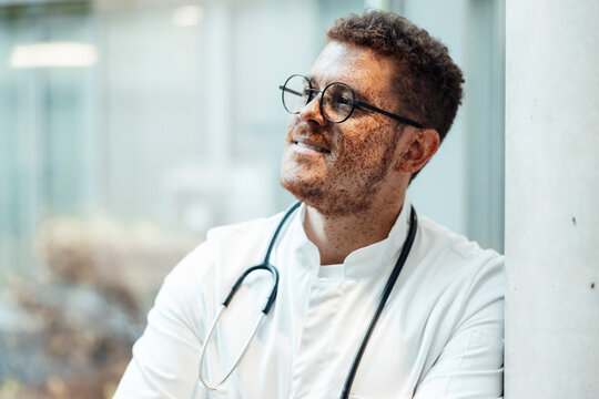 Doctor with freckles in white coat and stethoscope smiling indoors