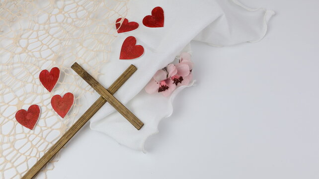 Una croce di legno con cuori rossi su tessuto bianco. Idea per San Valentino, con uno spazio vuoto per un biglietto d'amore
