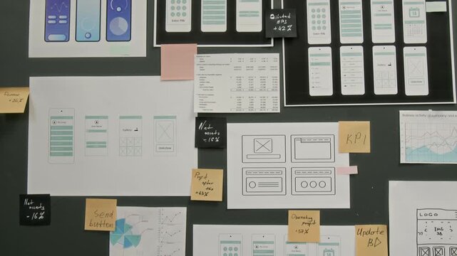 Close-up of printed pages with prototypes of wireframe layouts, displayed on gray wall at UX design company, in office of team developing innovative mobile smartphone application