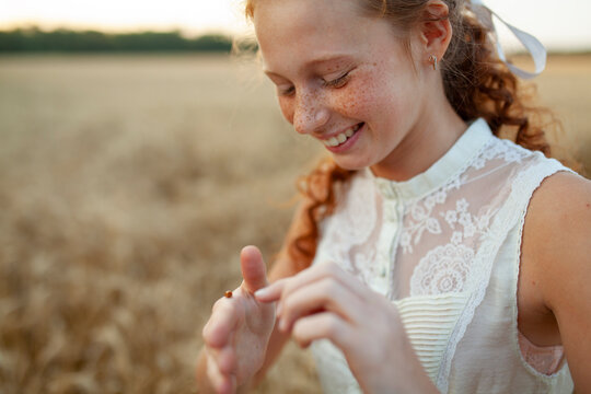 Smiling girl with red hair and freckles in wheat field at sunset