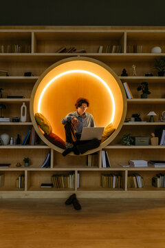 Person relaxing with laptop in illuminated round seat in library