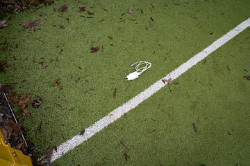 Charging cable lying on a green sports playground ground with a painted white line. Everyday tech object in a casual urban environment, themes of connectivity, technology, and modern lifestyle.