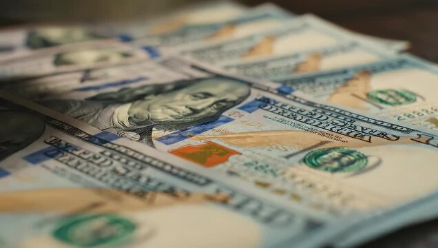 Stack of hundred dollar bills on wooden table. Close-up view shows detailed texture and design of currency. Concept of wealth, finance, and investment. Modern economy visual.