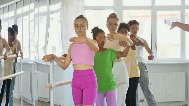 Adult woman teacher shows batman tandu jete movement to group of teenage boys and girls