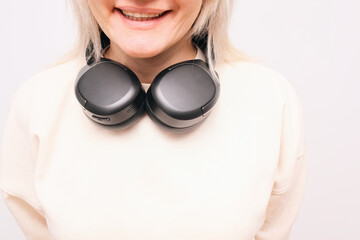 Smiling blonde woman with black wireless headphones around her neck.