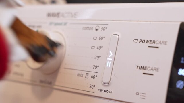 A close-up view of a dog paw placed on the dial of a white washing machine, appearing to interact with the control panel in a humorous indoor setting