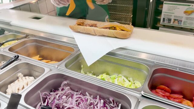 Fast Food Worker Preparing a Sub Sandwich with Fresh Ingredients