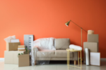Fototapeta premium Blurred view of sofa with stretch film and boxes near orange wall in room on moving day