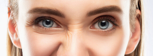 Blue eyes of a young woman close-up. On her face, mimic wrinkles are visible near the eyes and between the eyebrows.