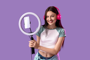 Teenage blogger in headphones recording video on lilac background
