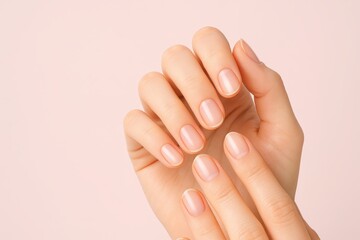 Close-up shot of a woman's hands with beautifully manicured nails, showcasing elegance and care against a soft, pastel pink background, highlighting natural beauty.