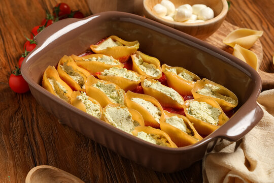 Baking dish of stuffed conchiglie pasta with cheese and tomatoes on wooden background