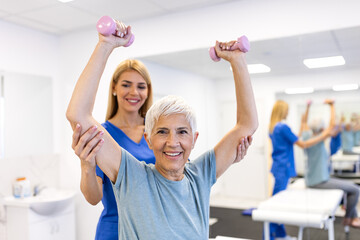 Happy senior woman lifting dumbbells with physiotherapist. Healthcare and medicine concept. Elderly patient doing strength training and rehabilitation exercises with female doctor in clinic office.