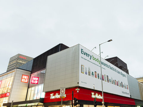 Manchester storefronts and a large Holland and Barrett billboard scene featuring Uniqlo and Tim Hortons on a busy street