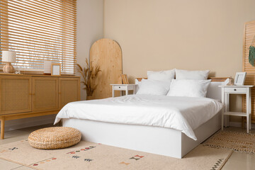 Cozy bed with white blanket and soft pillows in stylish bedroom