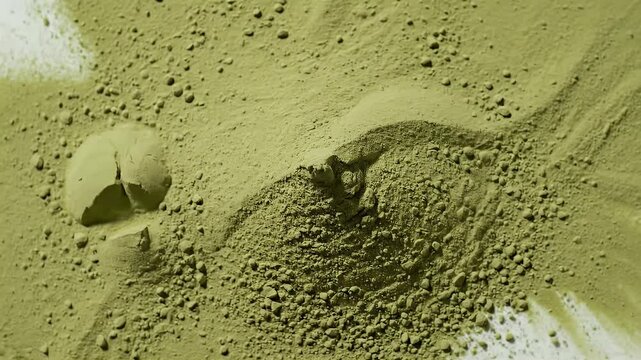 Green matcha powder texture with uneven surface and scattered particles.