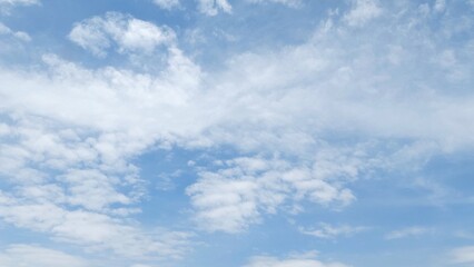 Fototapeta premium White fluffy clouds against a clear blue summer sky. Natural blue sky background with calm atmosphere. Blue sky texture background with soft and beautiful pattern.