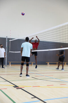 Four African American men in sportswear jumping and spiking multicolored volleyball over net in gym