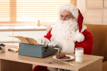 Santa Claus with typewriter, cookies and glass of milk writing Christmas story at home