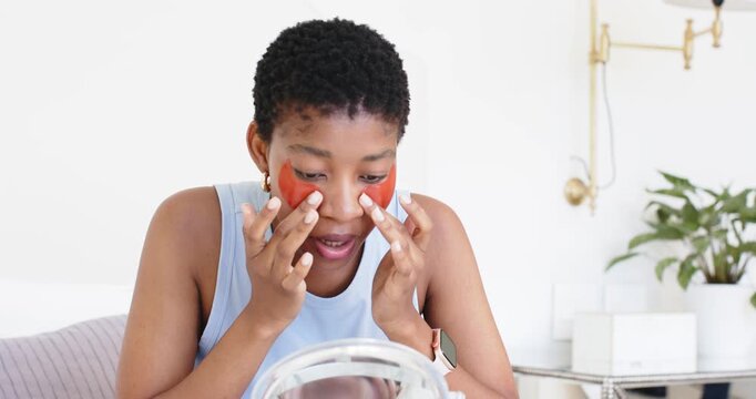 Woman leaning toward mirror, applying red hydrogel eye patches at vanity, pressing for hydration