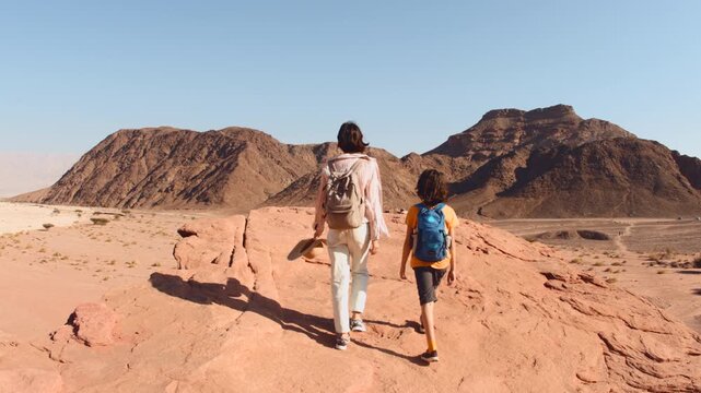 A mother and child on a hike. A happy teenage boy walks along a rocky trail in the desert next to his mother, enjoying the breathtaking view during their vacation. Trekking in the desert.