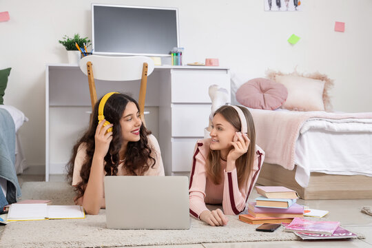 Female students with headphones using laptop in dorm room