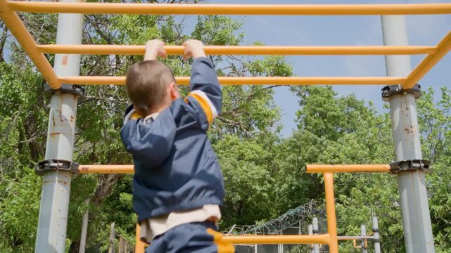  School Age Boy Crossing Yellow Monkey Bars at Park Playground. Medium shot of a determined boy in a tracksuit using monkey bars for strength training. 
