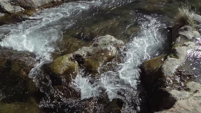 A rapid river flowing downstream is split into two paths by a large boulder in the water.